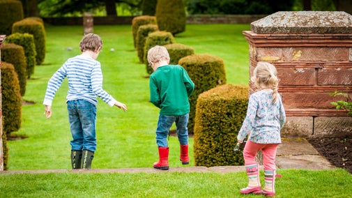 Three children, all wearing wellington boots are facing away from the camera as they walk down the stairs on the South Terrace at Wightwick Manor.